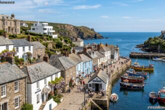 Traditional Cornwall houses overlooking a picturesque coastal harbor with fishing boats and scenic sea views.