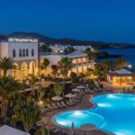 H10 Timanfaya Palace luxury resort at dusk with illuminated outdoor pools, elegant white architecture, palm trees, landscaped gardens, and scenic oceanfront views in Lanzarote.