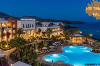 H10 Timanfaya Palace luxury resort at dusk with illuminated outdoor pools, elegant white architecture, palm trees, landscaped gardens, and scenic oceanfront views in Lanzarote.