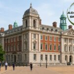 Old Admiralty Building in London showcasing its grand historic architecture with a landscaped walkway and visitors, featuring an "Old Admiralty Building" logo in the top-right corner.