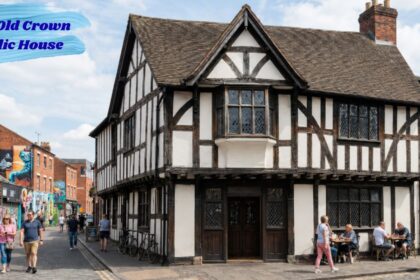 Historic The Old Crown Public House, a timber-framed Tudor-style building on a lively street with pedestrians, outdoor seating, and colorful murals in the background.