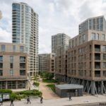 Modern view of the Stratford Halo Building residential development featuring a tall glass tower, contemporary apartment blocks, landscaped walkways, and surrounding urban architecture under a cloudy sky.