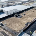 Aerial view of a built-up flat roof on a large commercial building with roofing workers, HVAC units, and multiple roofing layers.