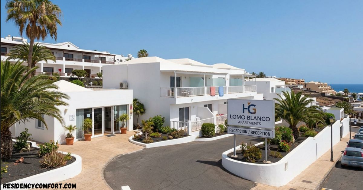 White Lomo Blanco Apartments complex with palm trees, landscaped gardens, balconies, and a reception sign, overlooking the ocean.