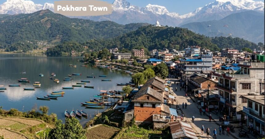 Aerial view of Pokhara Town beside a tranquil lake, colorful boats, hillside buildings, lush greenery, and snow-capped Himalayan mountains.