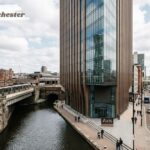 Axis Tower Manchester beside the canal and tram tracks, with city streets and historic brick buildings