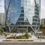 Building Eight modern glass office building with landscaped plaza and surrounding city buildings.