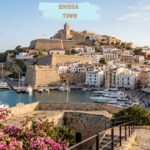 Eivissa Town historic hilltop buildings, stone fortress, harbor, and boats overlooking the Mediterranean Sea.