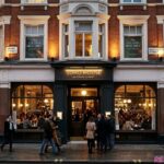 Soho House at 40 Greek Street in London, featuring historic architecture, a busy street, pedestrians, and red double-decker buses.