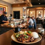 Teriyaki House restaurant interior with chef preparing a Japanese meal and a plated teriyaki chicken dish in the foreground.