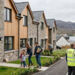 These Homes feature modern stone cottages with wooden cladding, surrounded by landscaped gardens and a scenic lakeside mountain view.